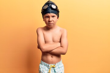 Cute blond kid wearing swimwear and swimmer glasses skeptic and nervous, disapproving expression on face with crossed arms. negative person.