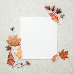 Autumn greeting card, thanksgiving day. White mockup paper sheet with foliage decoration on stone background. Copy space, flat lay