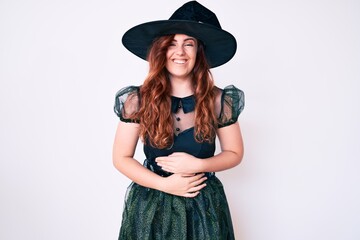 Young beautiful woman wearing witch halloween costume smiling and laughing hard out loud because funny crazy joke with hands on body.