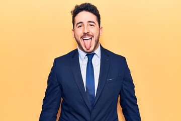 Young hispanic man wearing suit sticking tongue out happy with funny expression. emotion concept.