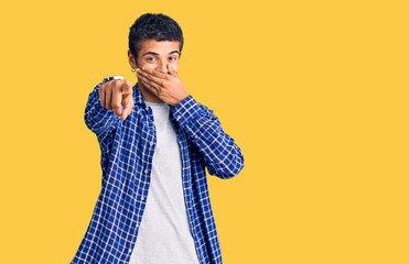 Young african amercian man wearing casual clothes laughing at you, pointing finger to the camera with hand over mouth, shame expression