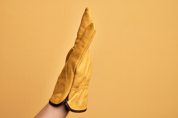 Hand of caucasian young man with gardener glove over isolated yellow background showing side of stretched hand, pushing and doing stop gesture