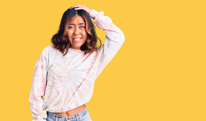 Young beautiful mixed race woman wearing casual tie dye sweatshirt confuse and wonder about question. uncertain with doubt, thinking with hand on head. pensive concept.