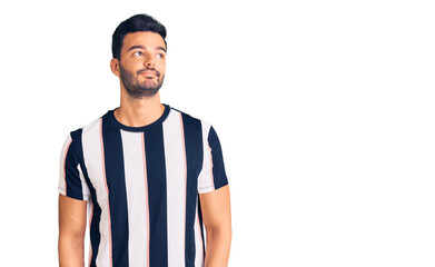 Young handsome hispanic man wearing striped tshirt smiling looking to the side and staring away thinking.