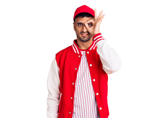 Young hispanic man wearing baseball uniform doing ok gesture with hand smiling, eye looking through fingers with happy face.