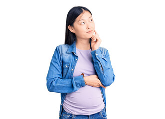 Young beautiful chinese woman pregnant expecting baby with hand on chin thinking about question, pensive expression. smiling and thoughtful face. doubt concept.