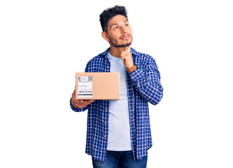 Handsome latin american young man holding delivery package serious face thinking about question...
