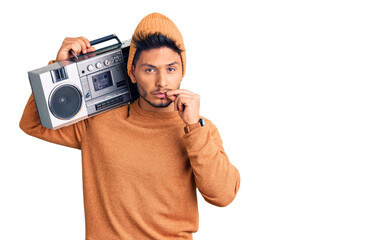 Handsome latin american young man holding boombox, listening to music mouth and lips shut as zip...