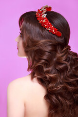 Naklejka premium Beautiful brunette woman with long Curly hair wearing crown decorated gemstones. Fashion makeup and hairstyle. Portrait of young gorgeous bride. Isolated on pink background