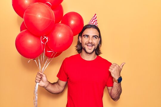 Young handsome man holding balloons pointing thumb up to the side smiling happy with open mouth