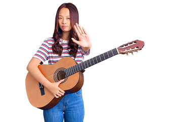 Fototapeta premium Young beautiful chinese girl playing classical guitar with open hand doing stop sign with serious and confident expression, defense gesture
