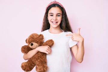 Cute hispanic child girl holding teddy bear pointing finger to one self smiling happy and proud