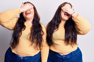 Young plus size twins wearing casual clothes smiling and laughing with hand on face covering eyes for surprise. blind concept.