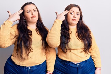 Young plus size twins wearing casual clothes shooting and killing oneself pointing hand and fingers to head like gun, suicide gesture.