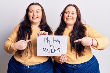 Young plus size twins holding my body my rules banner smiling happy pointing with hand and finger