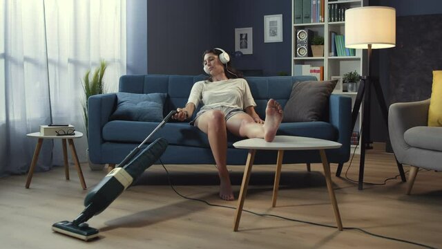 Lazy woman sitting on the sofa and vacuuming the floor