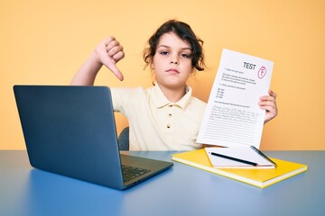 Cute hispanic child showing failed exam sitting on the desk with angry face, negative sign showing dislike with thumbs down, rejection concept