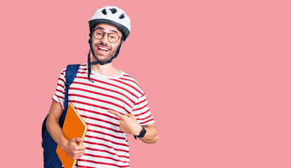 Young hispanic man wearing student backpack and bike helmet holding binder smiling happy pointing with hand and finger