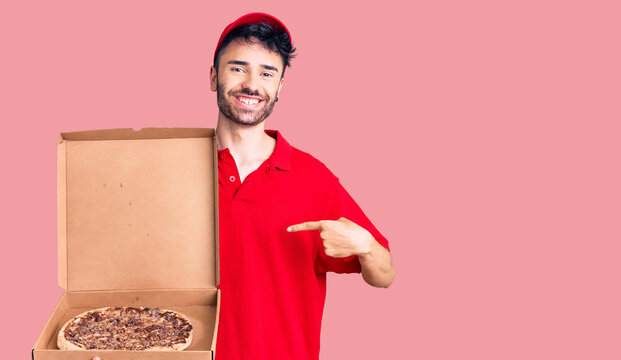Young hispanic man holding delivery pizza box pointing finger to one self smiling happy and proud