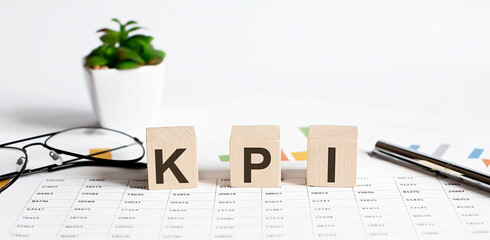 KPI word concept written on wooden blocks, cubes on a light table with flower ,pen and glasses on chart background