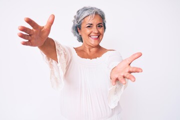 Senior hispanic grey- haired woman wearing casual clothes looking at the camera smiling with open arms for hug. cheerful expression embracing happiness.