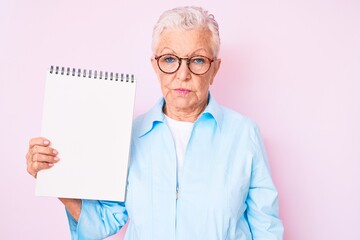 Senior beautiful woman with blue eyes and grey hair holding notebook thinking attitude and sober expression looking self confident