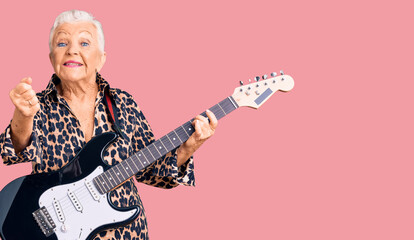 Senior beautiful woman with blue eyes and grey hair with modern look playing electric guitar screaming proud, celebrating victory and success very excited with raised arms