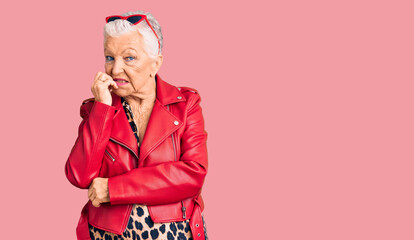 Senior beautiful woman with blue eyes and grey hair wearing a modern style with a red leather jacket looking stressed and nervous with hands on mouth biting nails. anxiety problem.
