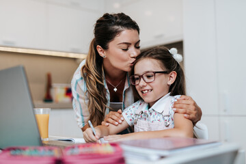 Beautiful young mother helping her younger daughter with homework.