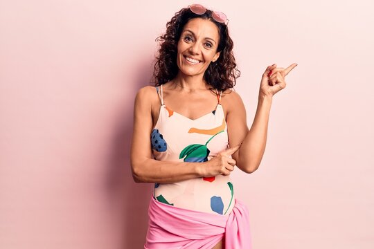 Middle age beautiful woman wearing swimwear and sunglasses smiling happy pointing with hand and finger to the side