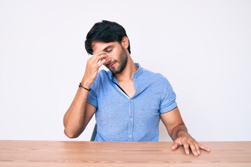 Handsome hispanic man wearing casual clothes sitting on the table tired rubbing nose and eyes feeling fatigue and headache. stress and frustration concept.