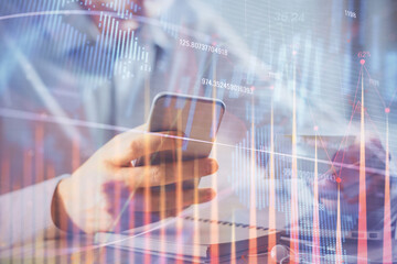 Double exposure of man's hands holding and using a phone and financial graph drawing. Analysis concept.