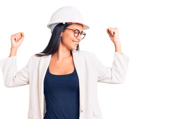 Young beautiful latin girl wearing architect hardhat and glasses showing arms muscles smiling proud. fitness concept.