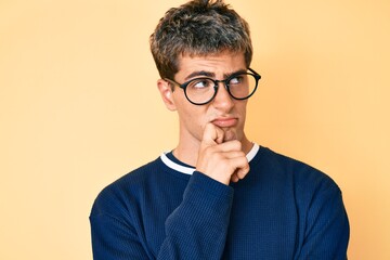 Young handsome man wearing casual clothes and glasses thinking concentrated about doubt with finger...