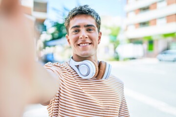 Young handsome caucasian man smiling happy wearing headphones making selfie by the camera walking at city.