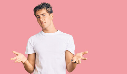 Young handsome man wearing casual white tshirt clueless and confused with open arms, no idea...