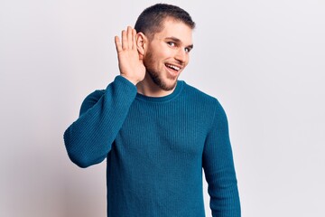 Young handsome man wearing casual sweater smiling with hand over ear listening and hearing to rumor or gossip. deafness concept.