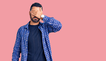 Fototapeta premium Young hispanic man wearing casual clothes covering eyes with hand, looking serious and sad. sightless, hiding and rejection concept
