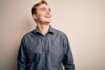Young handsome redhead man wearing casual shirt standing over isolated white background looking away to side with smile on face, natural expression. Laughing confident.