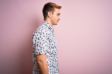 Young handsome redhead man wearing casual summer shirt standing over pink background looking to side, relax profile pose with natural face with confident smile.