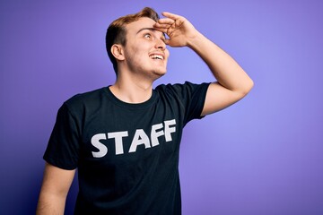 Fototapeta na wymiar Young handsome redhead worker man wearing staff t-shirt uniform over purple background very happy and smiling looking far away with hand over head. Searching concept.