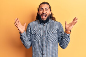 Naklejka premium Young arab man wearing casual clothes celebrating victory with happy smile and winner expression with raised hands