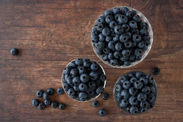 Top view of fresh blueberries in three glass bowls on a rustic wood table, berries spilled on table
