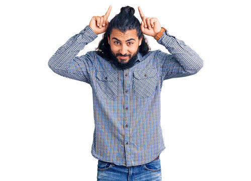 Young arab man wearing casual clothes doing funny gesture with finger over head as bull horns
