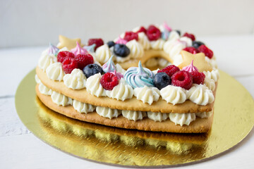 Delicious heart-shaped cake with meringue and fresh raspberries and blueberries on a white plate.