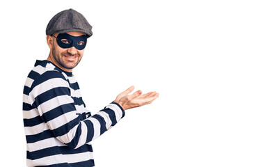 Young handsome man wearing burglar mask pointing aside with hands open palms showing copy space, presenting advertisement smiling excited happy
