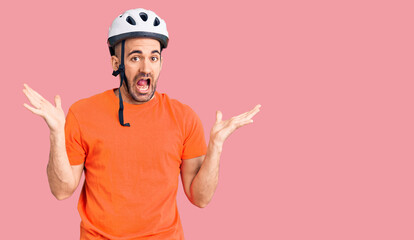 Young handsome man wearing bike helmet celebrating victory with happy smile and winner expression with raised hands