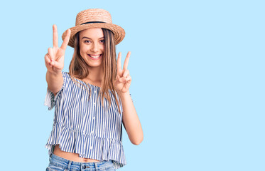 Obraz na płótnie Canvas Young beautiful girl wearing hat and t shirt smiling looking to the camera showing fingers doing victory sign. number two.