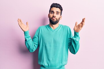 Young handsome man with beard wearing casual sweater clueless and confused with open arms, no idea...