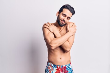 Fototapeta na wymiar Young handsome man with beard shirtless wearing swimwear hugging oneself happy and positive, smiling confident. self love and self care